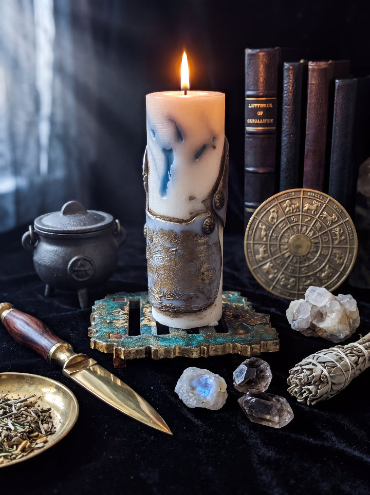 Lit Break the Seal candle on a green and gold resin stand, surrounded by antique books, crystals, a small cauldron and a zodiac wheel.
