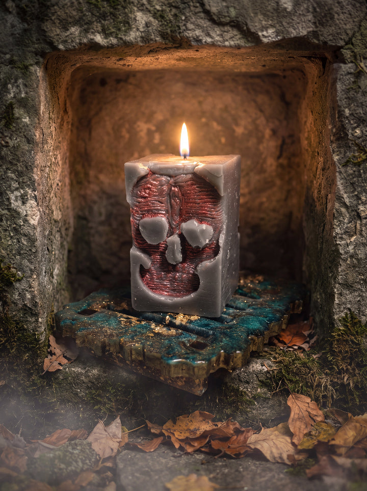 Lit Inner Demon beeswax skull candle on a green and gold resin stand inside a weathered stone niche with autumn leaves.