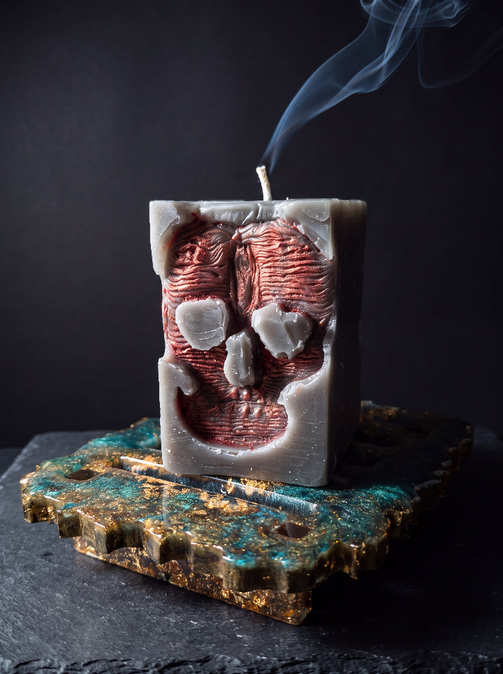 Close-up of Inner Demon candle with bronze skull relief and smoke rising from its wick, on a green and gold resin stand.