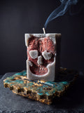 Close-up of Inner Demon candle with bronze skull relief and smoke rising from its wick, on a green and gold resin stand.