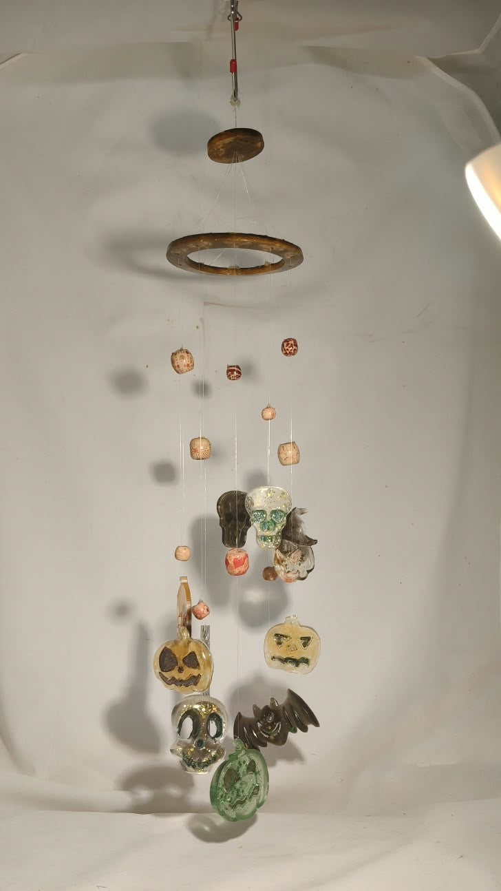 Full view of “Whispers of Samhain” resin wind chime with a circular frame, decorative beads and hanging Halloween charms against a light wall.