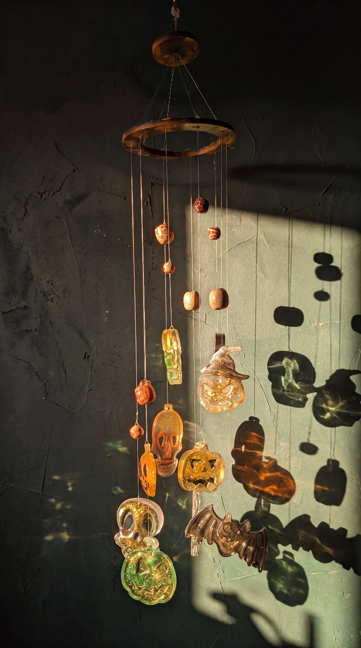 “Whispers of Samhain” resin suncatcher casting pumpkin, skull and bat-shaped shadows on a wall in sunlight.