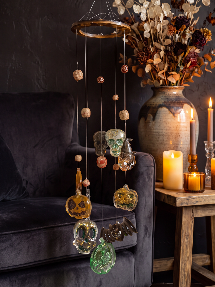 “Whispers of Samhain” resin wind chime with translucent Halloween charms, displayed beside a dark sofa and autumn flowers.