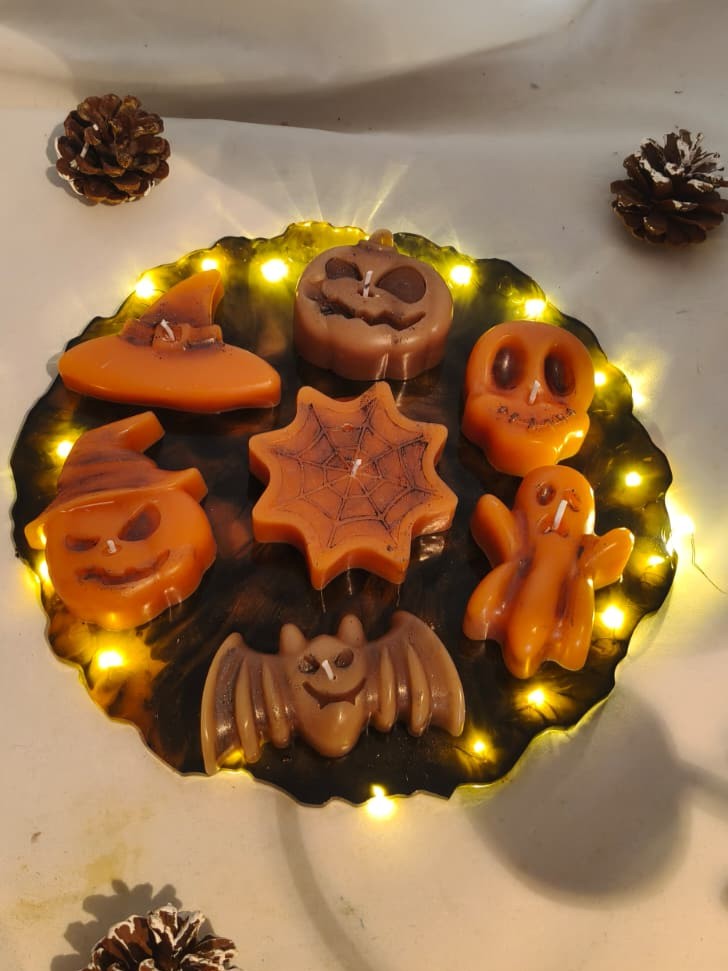 Close-up of seven Spellbound Halloween beeswax candles shaped as a witch hat, pumpkins, skull, spiderweb, ghost and bat on an LED resin stand.