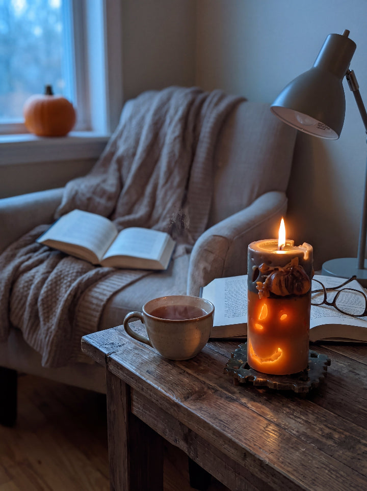 Lit Witch’s Harvest beeswax candle beside an open book and tea in a cosy reading corner.