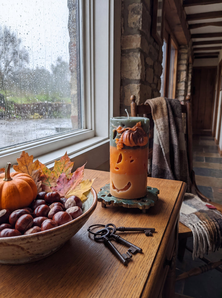Witch’s Harvest candle beside a rain-speckled window with chestnuts, autumn leaves and vintage keys.